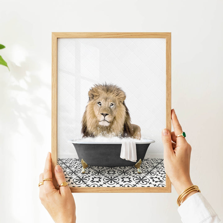 A person's hands are holding a framed picture of a lion sitting in a bathtub filled with bubbles.