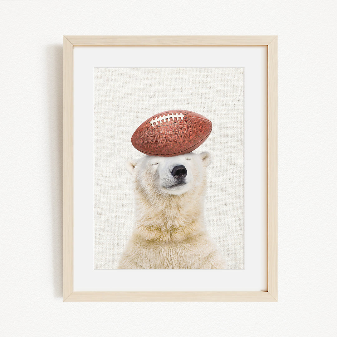A polar bear is sitting on top of a football, with its eyes closed, in a framed image.