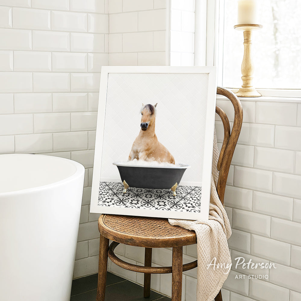 A framed image of a horse sitting in a bathtub, surrounded by a patterned tile floor, is displayed on a wooden chair in a bathroom setting.