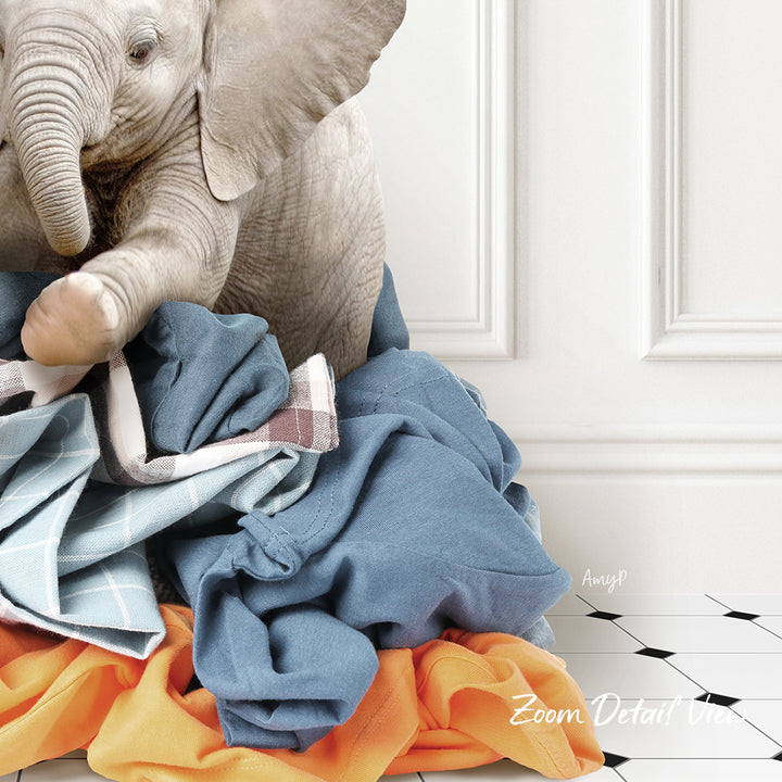 A baby elephant sitting on a pile of clothes, with a white wall and black and white checkered floor in the background.