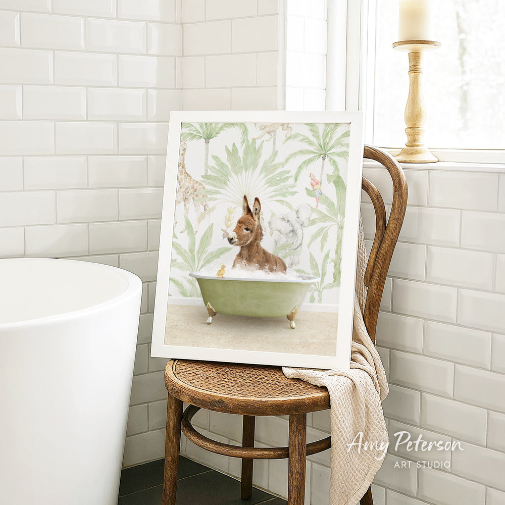 A framed painting of a dog sitting in a bathtub, surrounded by tropical foliage, is displayed on a wooden chair in a bathroom setting.