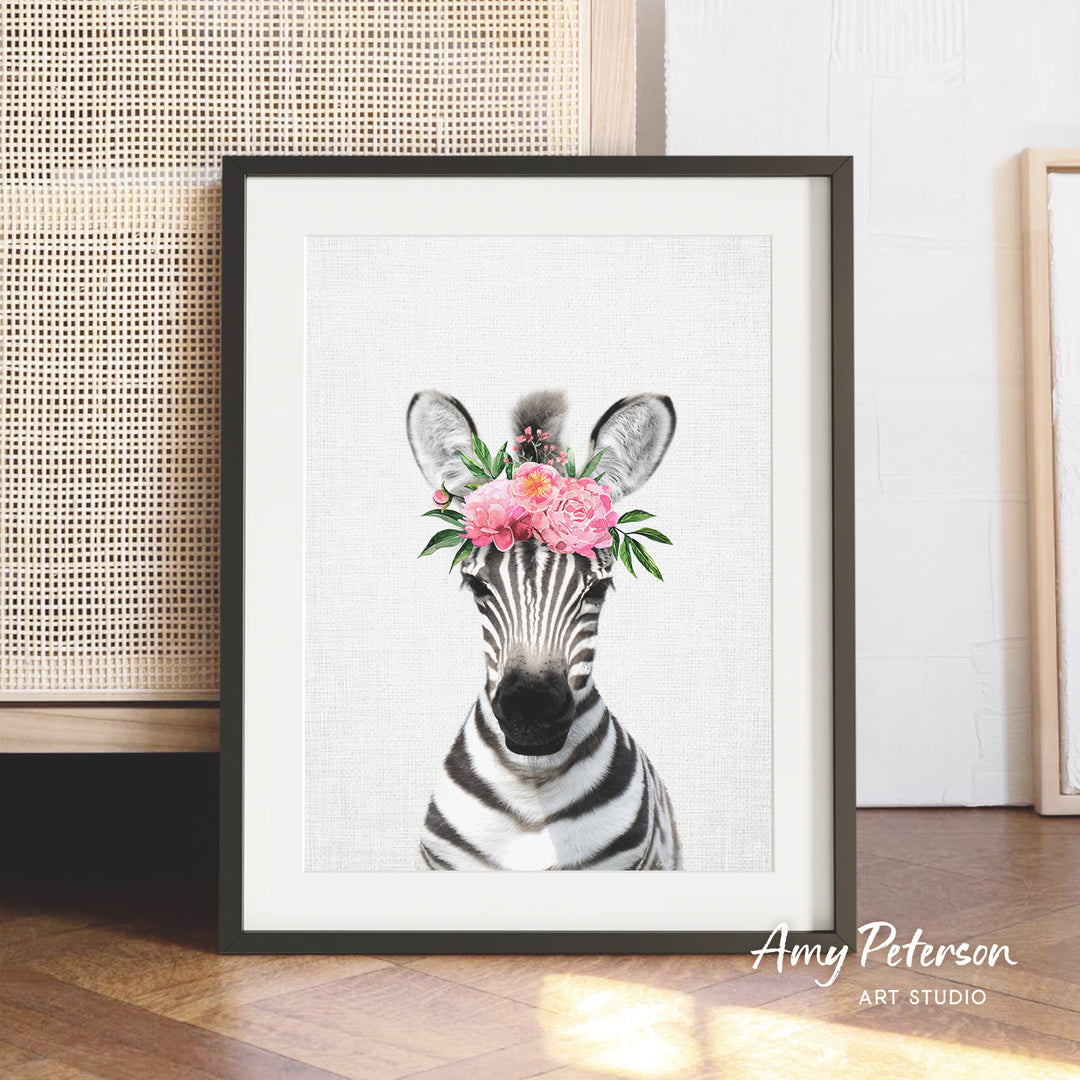 A framed print of a zebra with a floral headpiece is displayed on a wooden floor against a white wall.