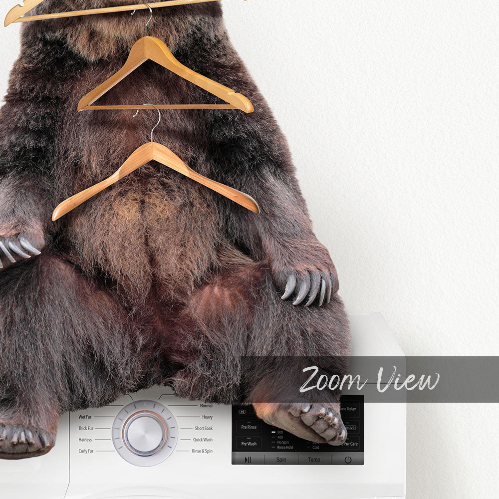 A stuffed bear sitting on a washing machine with clothes hangers hanging from it.