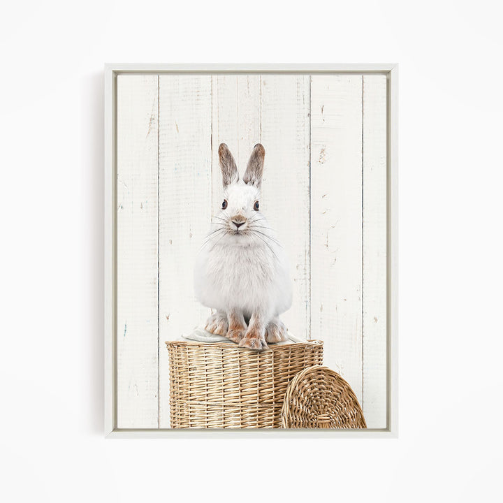 A white rabbit sits on a wicker basket against a white wooden background.