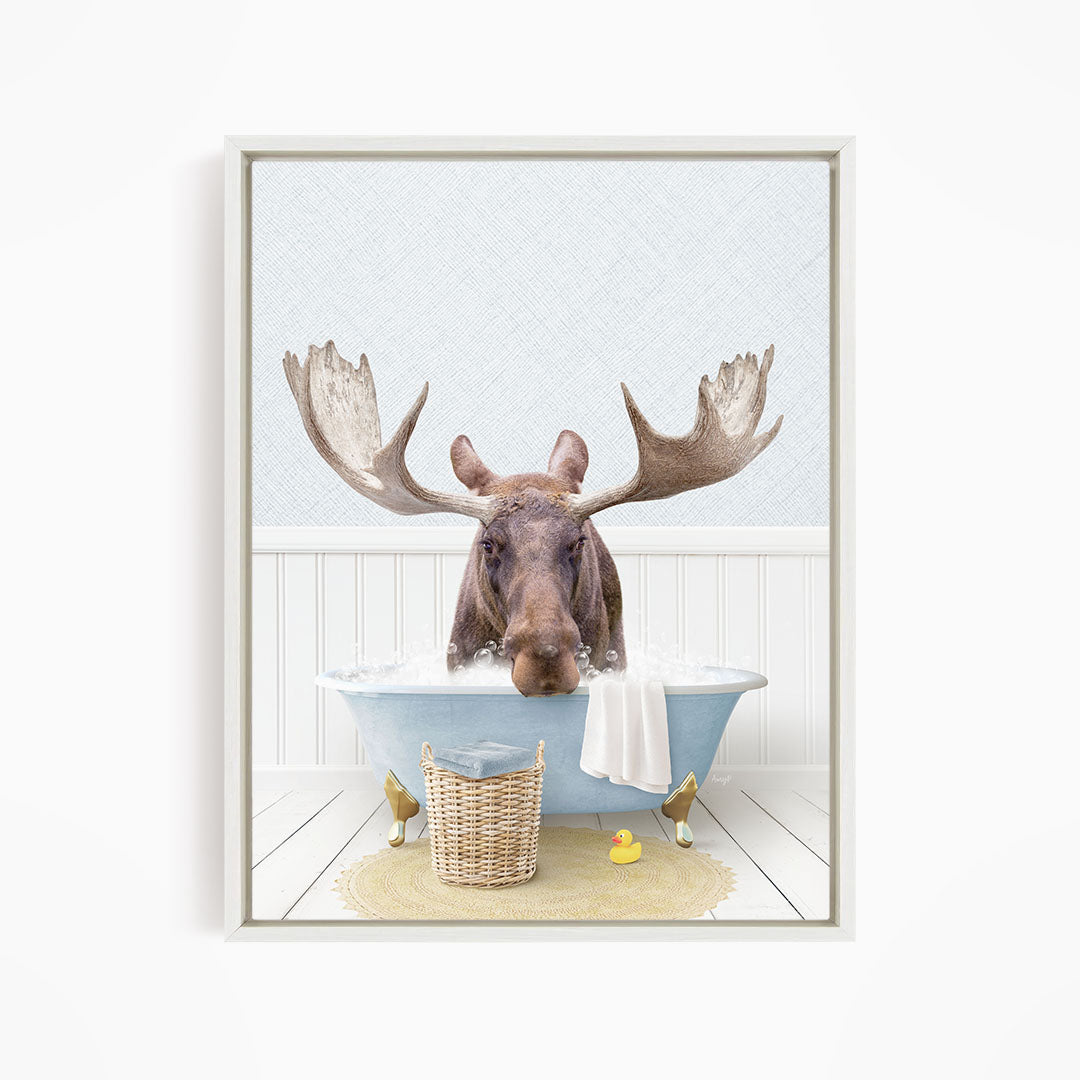A moose with large antlers is sitting in a blue bathtub filled with water, surrounded by a yellow rubber duck and a basket.