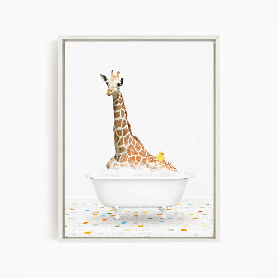 A giraffe is sitting in a white bathtub filled with bubbles, with a yellow rubber duck floating on the water.