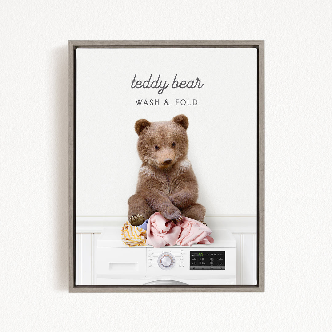 A teddy bear sitting on a white washing machine, with clothes and other laundry items around it.