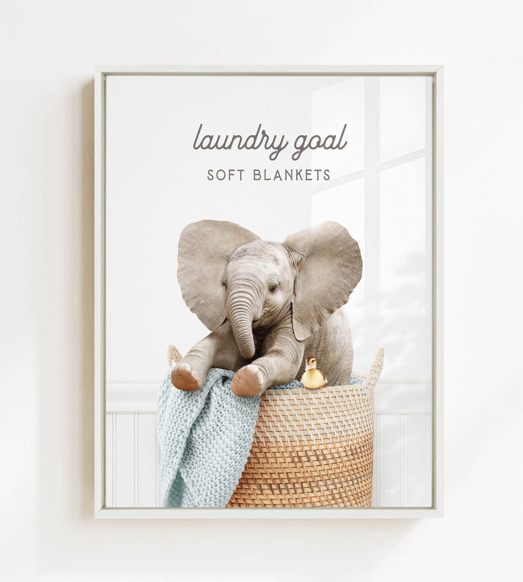 A baby elephant sitting in a woven basket, with a blanket and a small toy animal nearby.