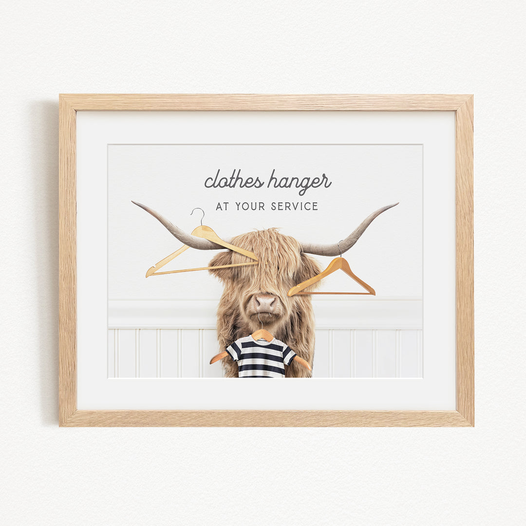A framed image depicting a large, furry animal with long horns, wearing a striped shirt and holding a clothes hanger in its mouth.