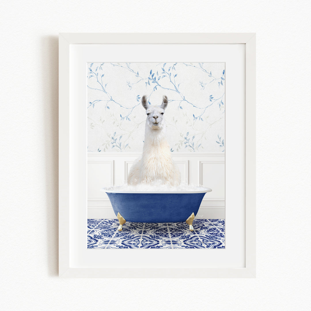 A white llama sitting in a blue bathtub filled with bubbles, with a blue and white floral patterned wall behind it.