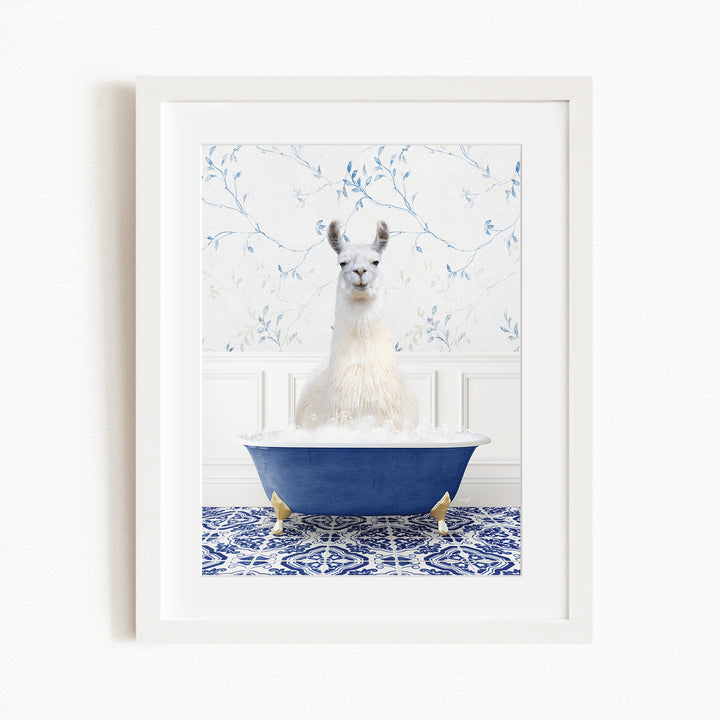 A white llama sitting in a blue bathtub filled with bubbles, with a blue and white floral patterned wall behind it.