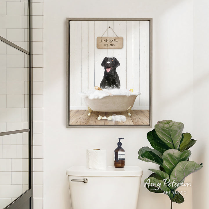 A framed image of a black dog sitting in a bathtub, with a sign above it that says "Hot Bath is Fun". The image is displayed in a bathroom setting, with a toilet and a potted plant visible.