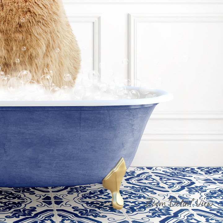 A fluffy brown cat is sitting in a blue bathtub filled with bubbles, with a gold claw-like object on the floor.