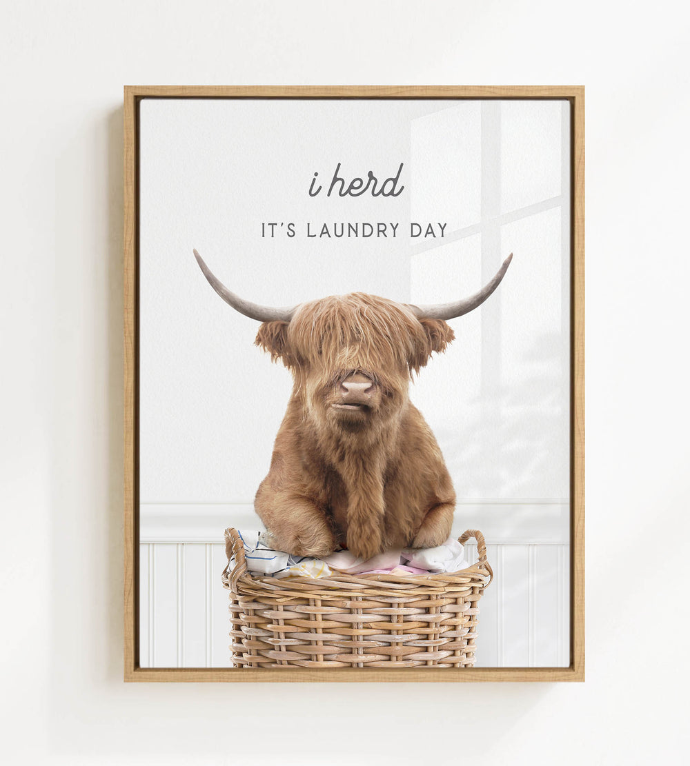 A brown cow with long horns is sitting in a wicker basket, with the text "i herd, it's laundry day" displayed above the image.