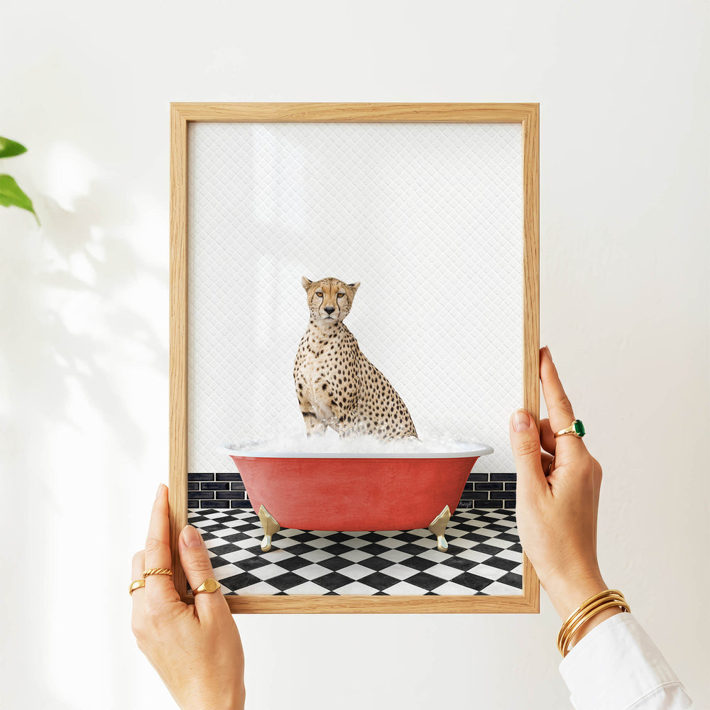 A person's hands are holding a framed picture of a cheetah sitting in a red bathtub filled with water, creating a whimsical and playful scene.
