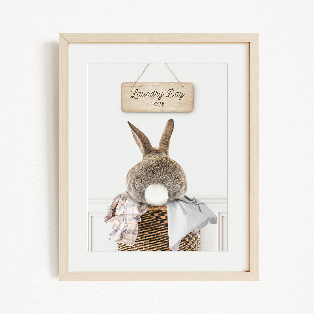 A framed image of a rabbit sitting in a basket, with a wooden sign above it that says "Laundry Day".
