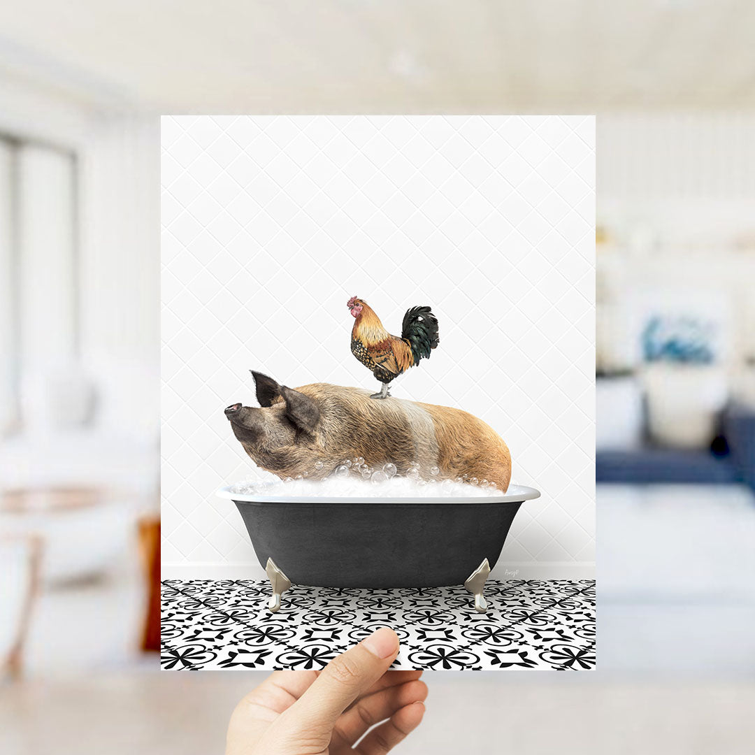 A hand holds up a framed image depicting a pig sitting in a bathtub, with a rooster perched on its back.