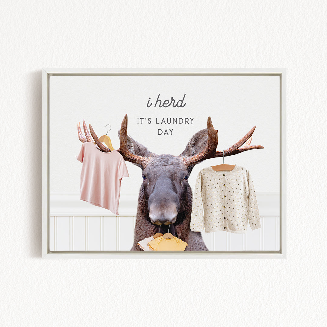 A framed image depicting a moose with antlers holding clothes, accompanied by the text "i herd, it's laundry day"
