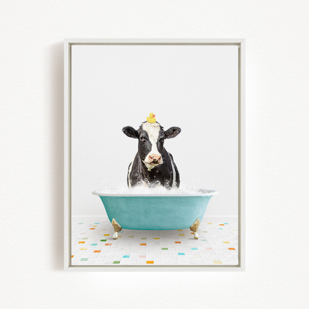 A black and white cow is sitting in a blue bathtub filled with bubbles, with a yellow rubber duck perched on its head.