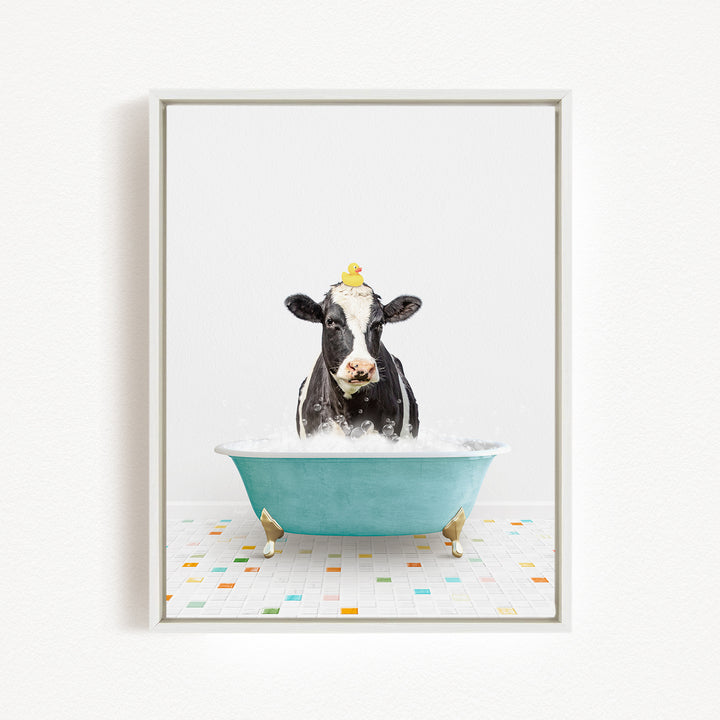 A black and white cow is sitting in a blue bathtub filled with bubbles, with a yellow rubber duck perched on its head.