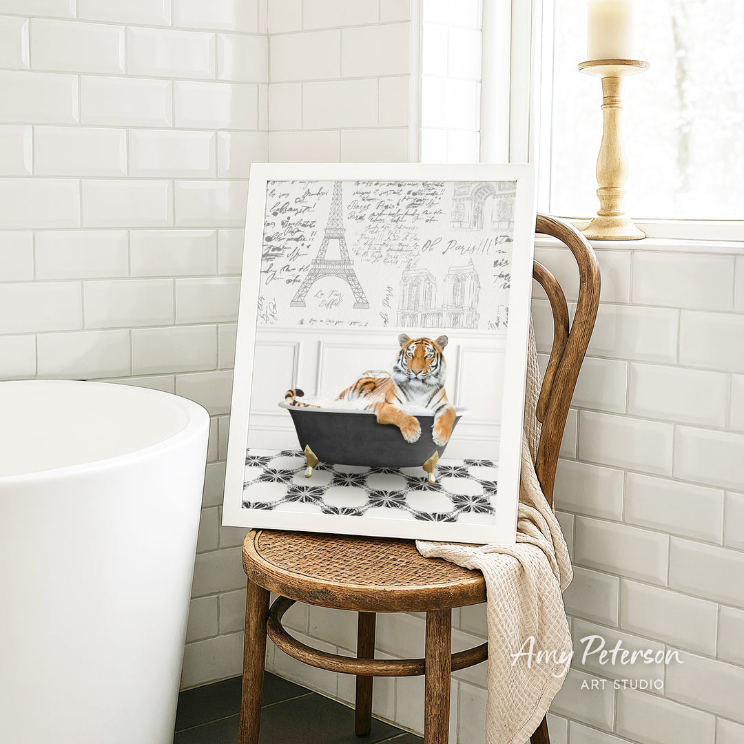 A framed print of a tiger sitting in a bathtub is displayed on a wooden chair in a bathroom setting.