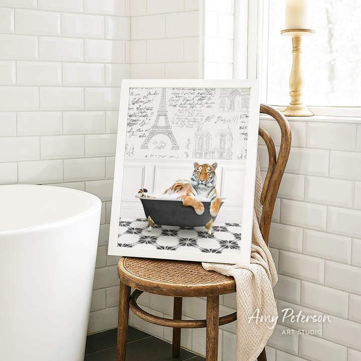 A framed print of a tiger sitting in a bathtub is displayed on a wooden chair in a bathroom setting.