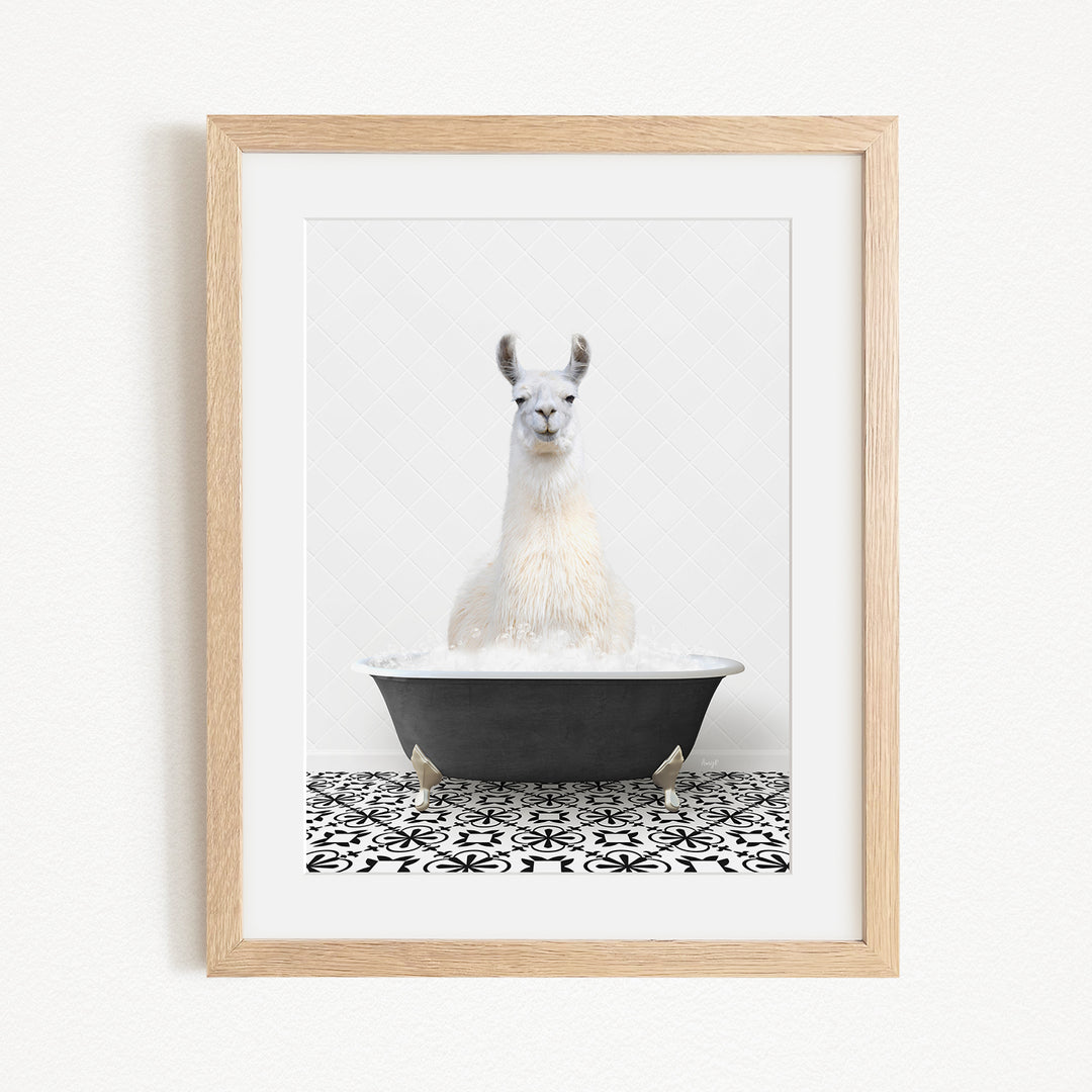 A white llama sitting in a black bathtub filled with bubbles, with a black and white patterned tile floor beneath it.