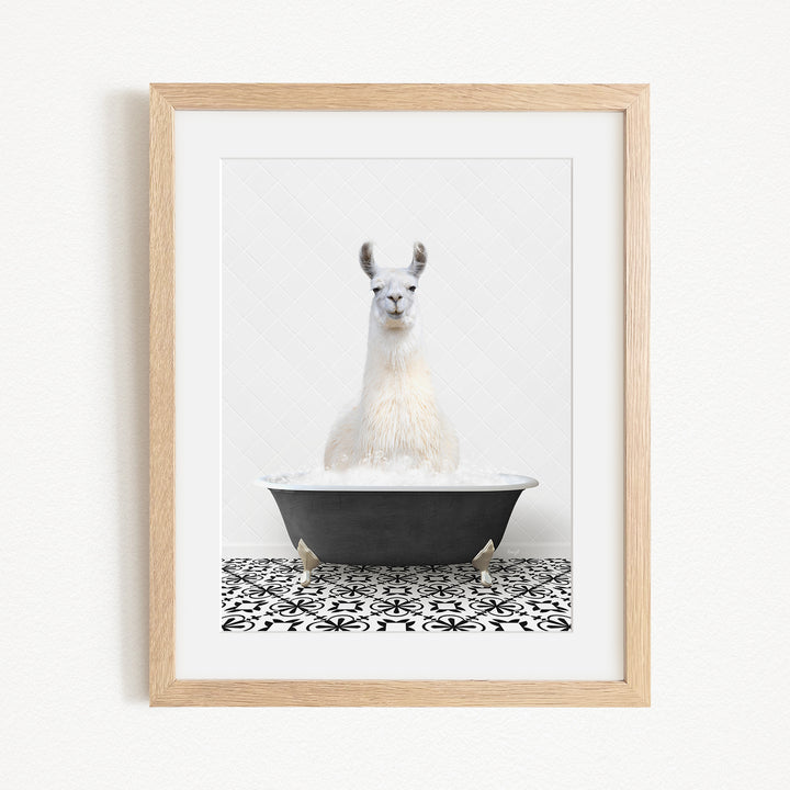 A white llama sitting in a black bathtub filled with bubbles, with a black and white patterned tile floor beneath it.