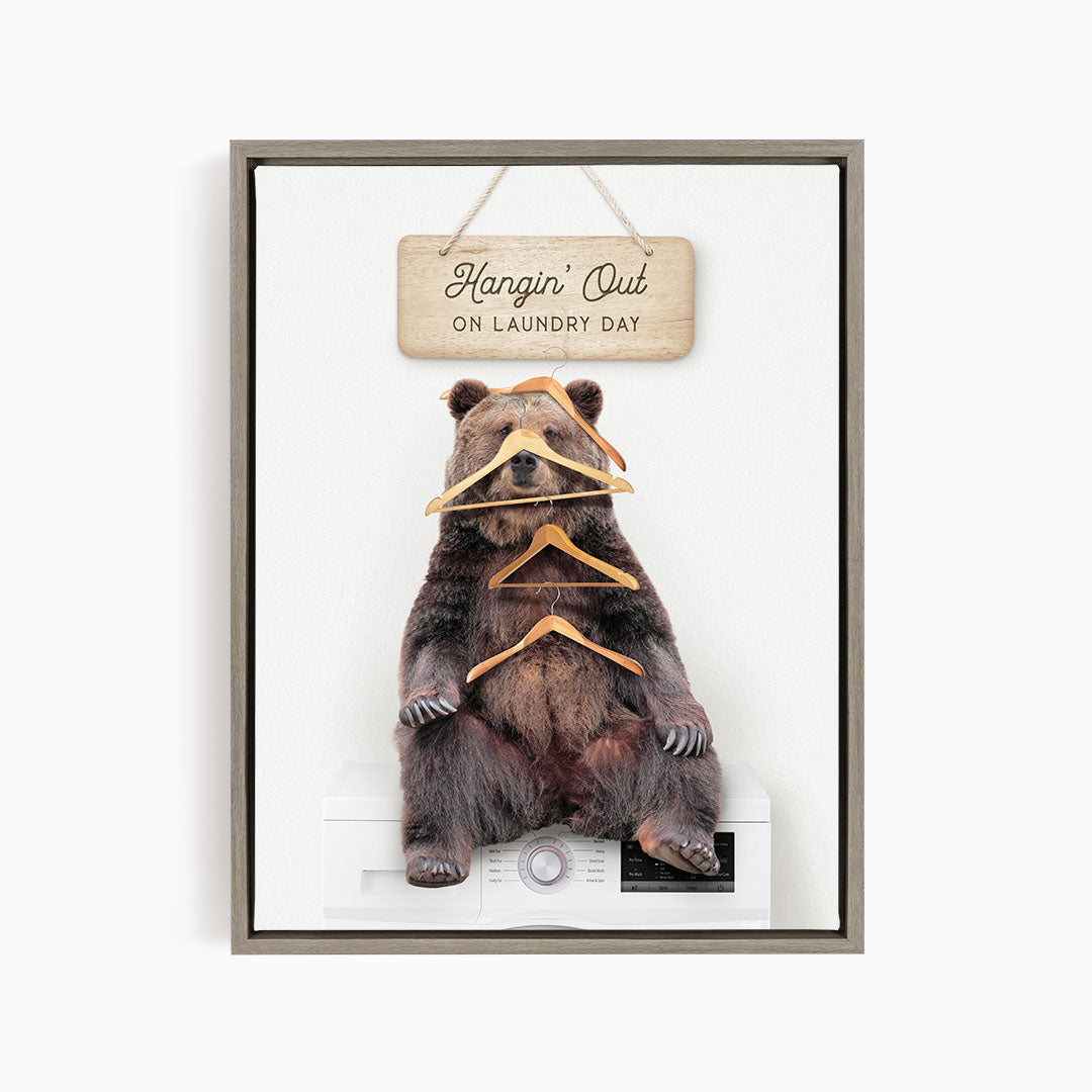 A framed image of a bear sitting on a washing machine, with a wooden sign above it that says "Hangin' Out on laundry day".