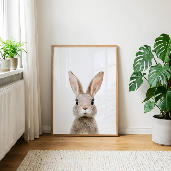 a large framed picture of a rabbit, which is the central focus of the room. The rabbit is positioned in the center of the frame, and the picture is hanging on a white wall. The room has a wooden floor and is decorated with potted plants and a rug.