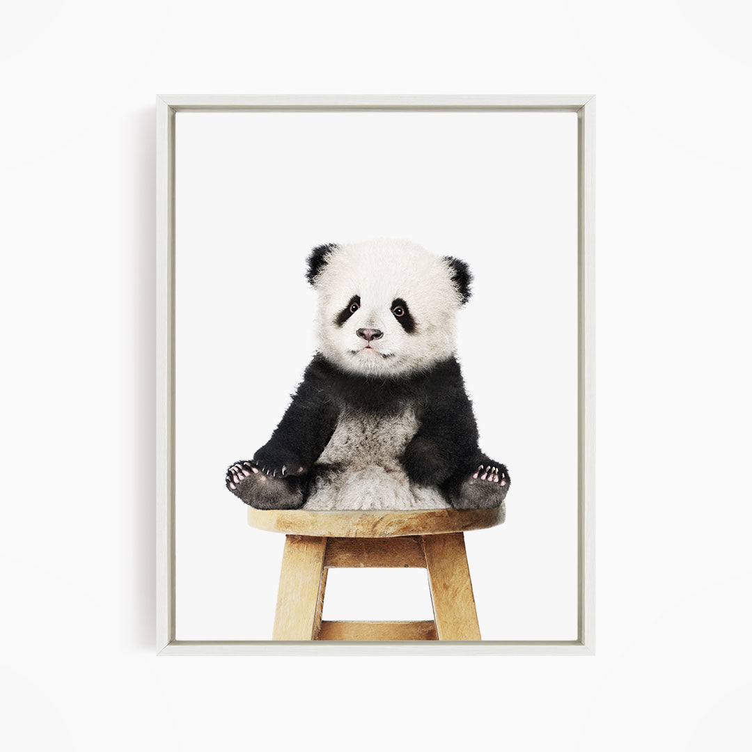A cute panda sitting on a wooden stool against a white background.