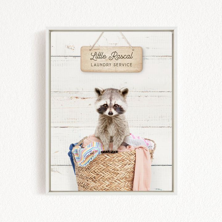 A raccoon sitting in a woven laundry basket, with a sign above it that reads "Little Racal Laundry Service".