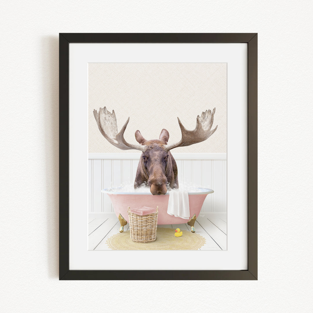A moose with large antlers is sitting in a pink bathtub, surrounded by a yellow rubber duck and a basket.