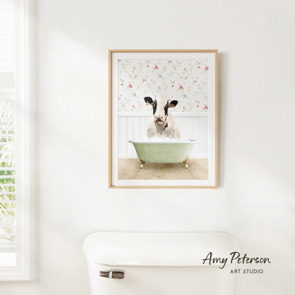A framed image of a cow sitting in a bathtub, with a floral pattern on the wall behind it.