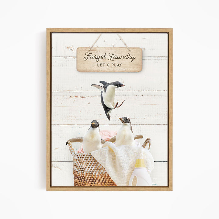A framed image depicting three penguins in a basket, with a sign that says "Forget Laundry, Let's Play" hanging above them.