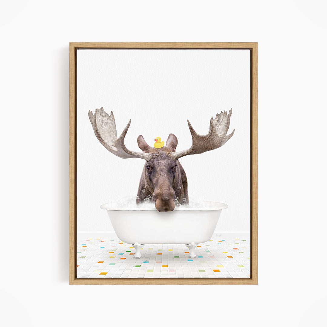 A moose with large antlers is sitting in a white bathtub, with a rubber duck perched on its head.