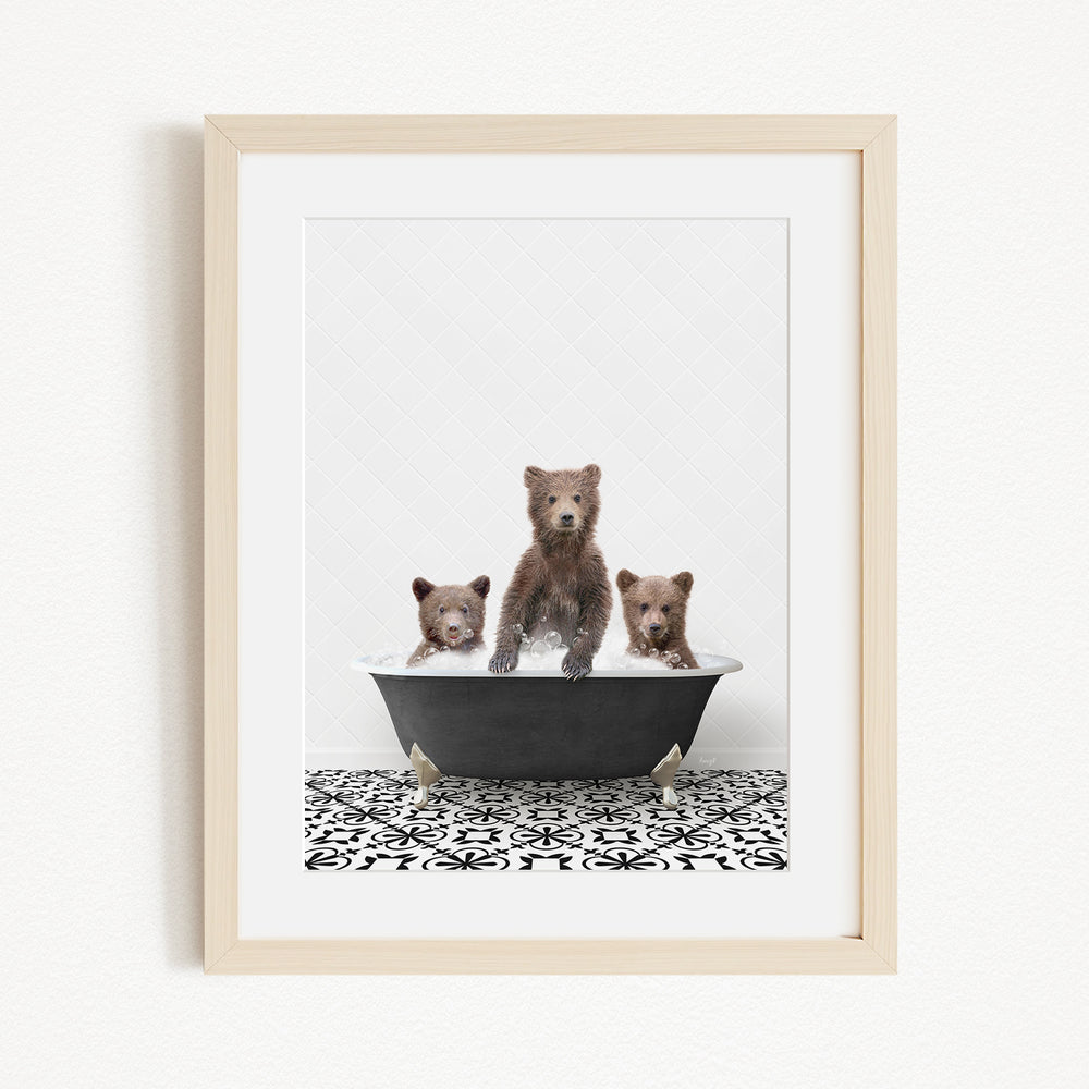 A framed image depicting three brown bears sitting in a black bathtub, with one bear standing on its hind legs and the other two sitting comfortably.