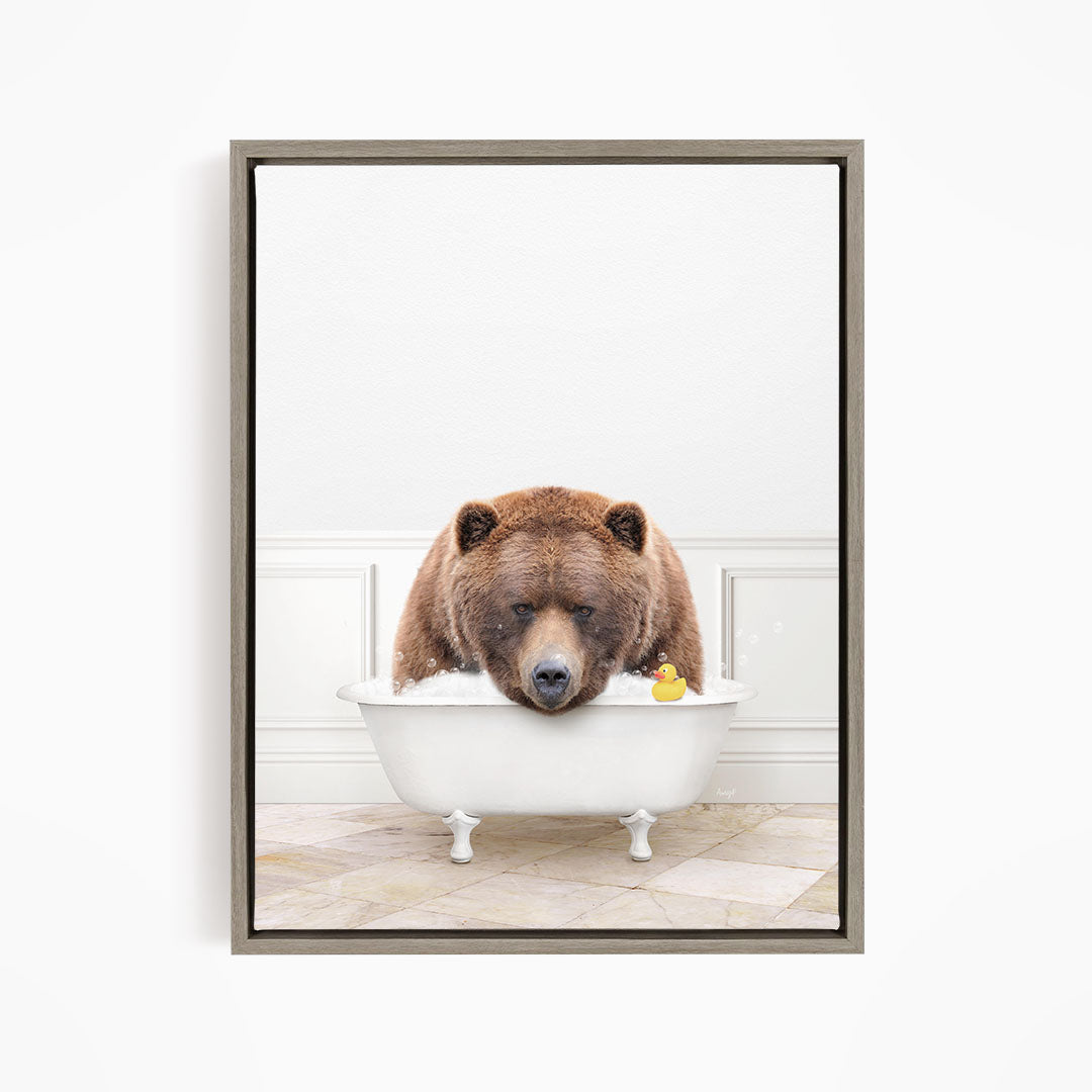 A brown bear is sitting in a white bathtub, with a yellow rubber duck floating in the water.