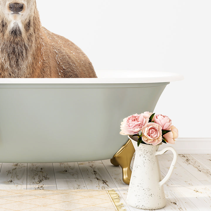A brown bear is sitting in a green bathtub, with a vase of pink flowers next to it on a white floor.