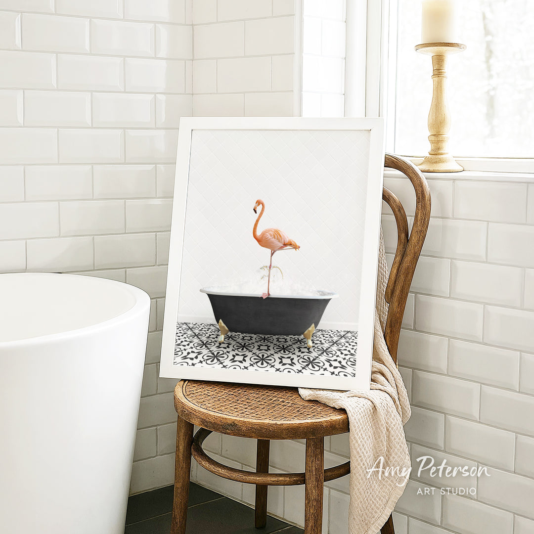 A framed image of a pink flamingo standing in a black bathtub, placed on a wooden chair in a bathroom setting.