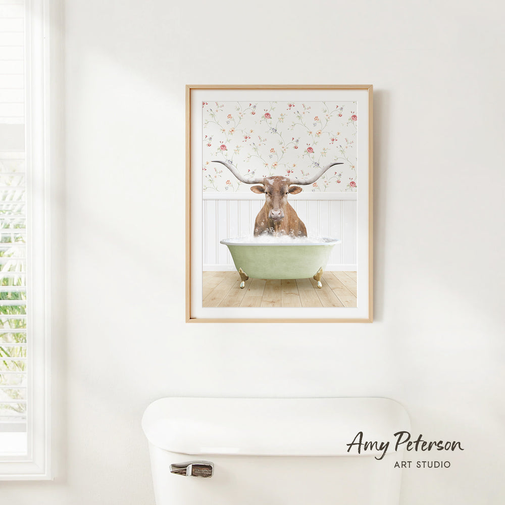 A framed image of a bull with horns sitting in a bathtub, set against a floral wallpaper background.