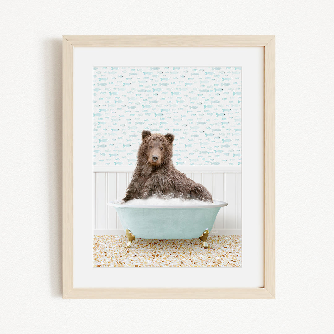 A brown bear sitting in a blue bathtub filled with bubbles, with a patterned wall behind it.