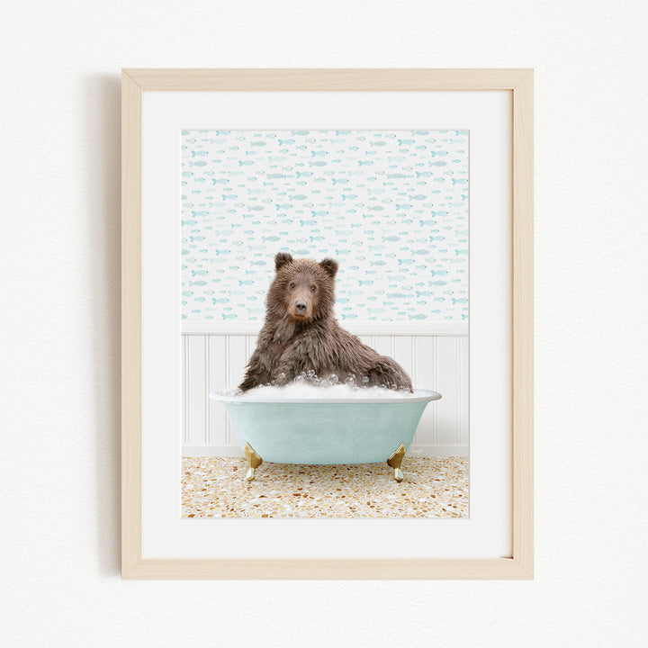 A brown bear sitting in a blue bathtub filled with bubbles, with a patterned wall behind it.