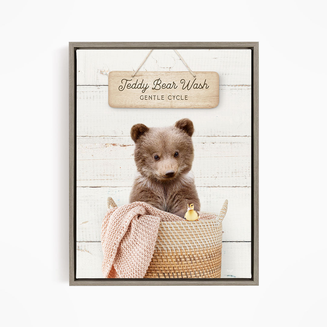 A teddy bear sitting in a woven basket, with a sign above that reads "Teddy Bear Wash Gentle Cycle".