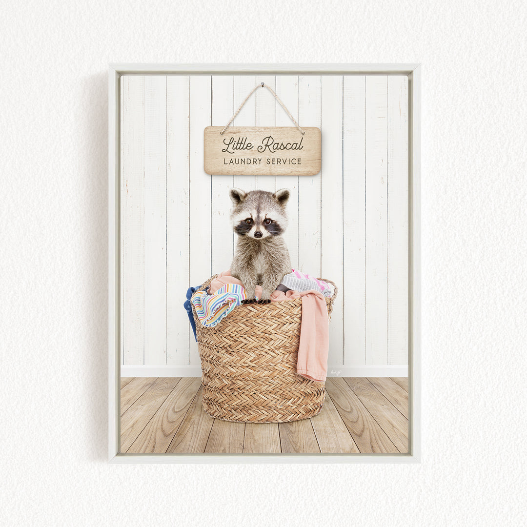 A raccoon sitting in a woven laundry basket, with a sign for "Little Racal Laundry Service" hanging above it.