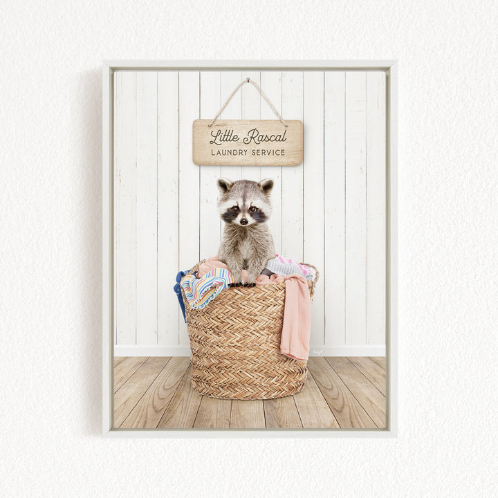 A raccoon sitting in a woven laundry basket, with a sign for "Little Racal Laundry Service" hanging above it.