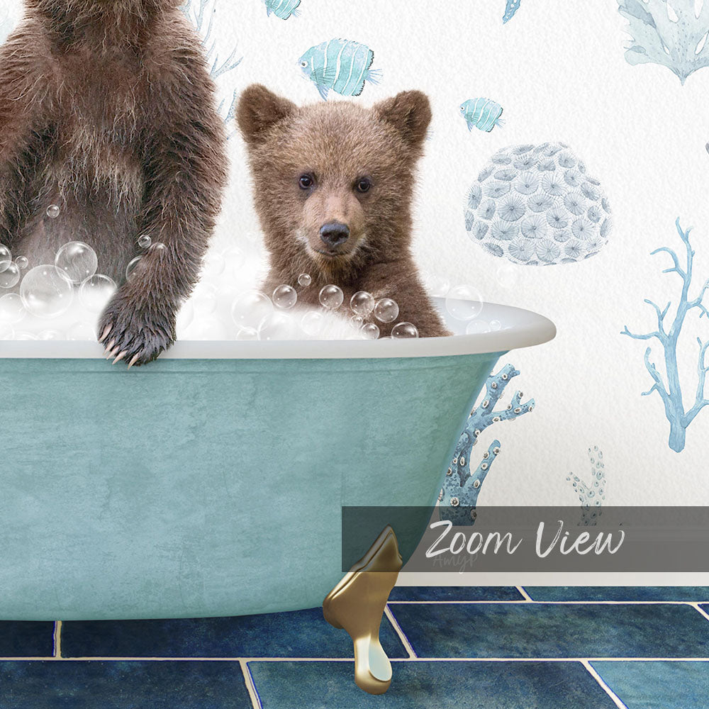 A baby bear sitting in a bathtub filled with bubbles, with a wall decorated with blue and white fish and coral designs behind it.