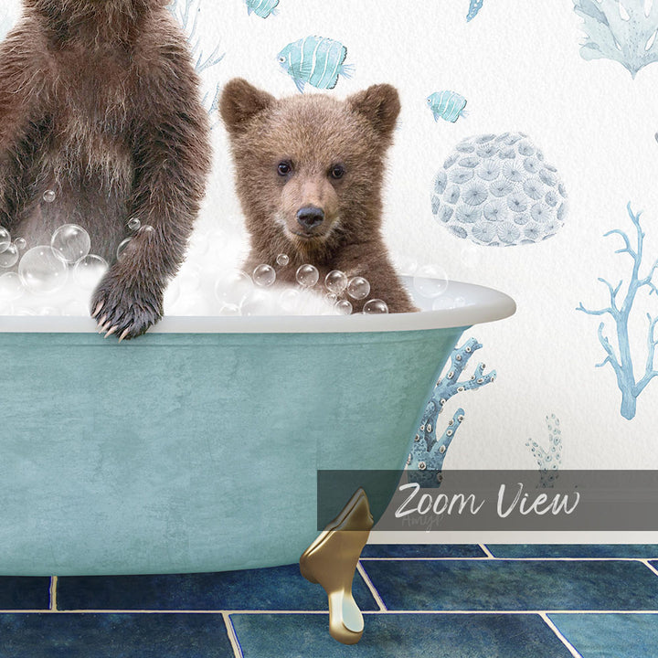 A baby bear sitting in a bathtub filled with bubbles, with a wall decorated with blue and white fish and coral designs behind it.