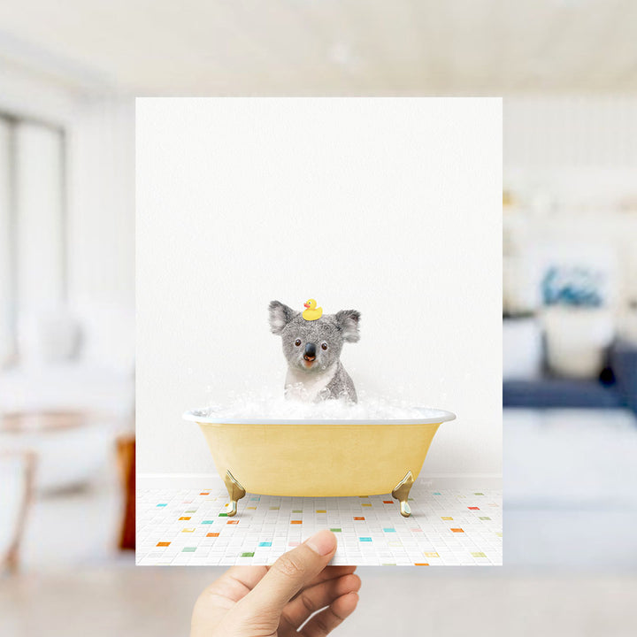A small gray dog is sitting in a yellow bathtub filled with bubbles, wearing a yellow rubber duck hat.