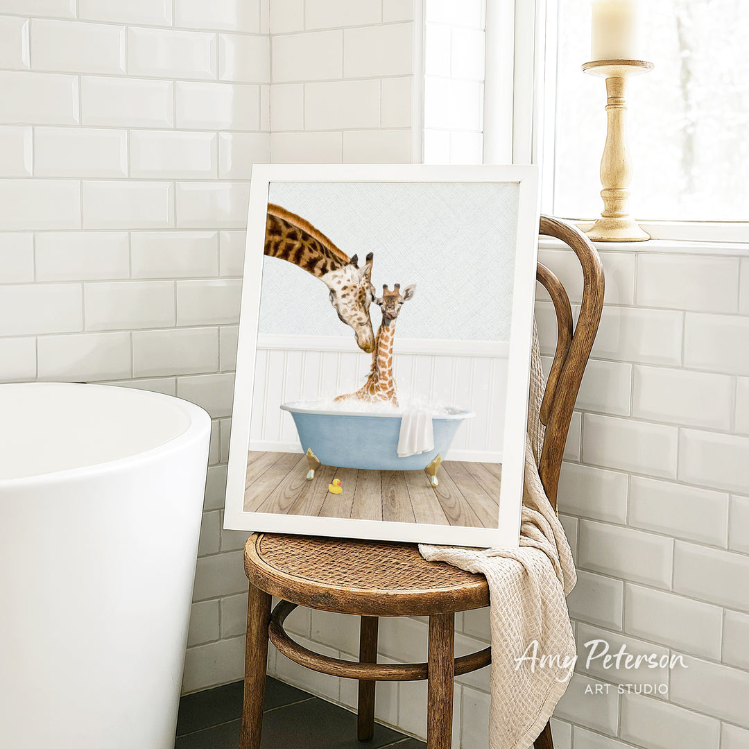 A framed image of a giraffe and a baby giraffe sitting in a bathtub, with a towel draped over the back of the chair.